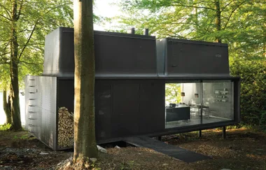 Modern black cabin with large glass windows in a forest setting.