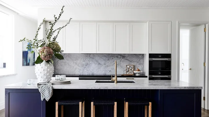 Modern kitchen with white cabinets and navy island base and Miele ovens