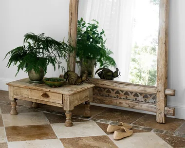 Rustic mirror with green panel beside table holding plants and rooster figurine, on checkered tile floor.
