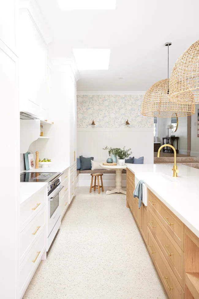 Bright kitchen with wooden and white cabinets, a large island, gold fixtures, rattan pendant lights, and a cozy nook.