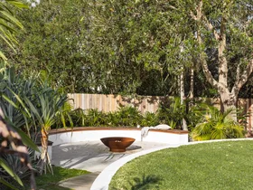 Coastal, tropical garden with curved wall, fence and lawn.