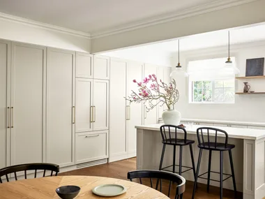 A modern neutral kitchen with shaker style cabinets, an island and timber table.