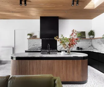 Modern kitchen with wood accents, marble countertops, and a central island with a vase of colorful leaves.