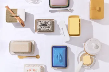 Various butter dishes and blocks of butter styled on a white surface.