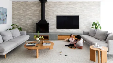 A modern living room with grey sofas, a fireplace, and a father playing with his daughter on the carpet.