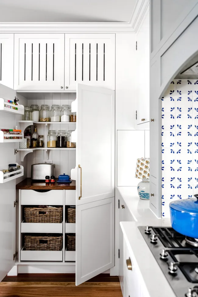 A white open pantry with rattan baskets and shelving.