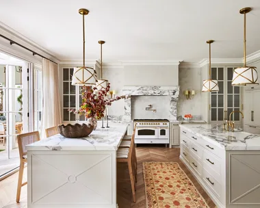 A large classic-style kitchen with two marble islands, a freestanding cooker and hanging lights.