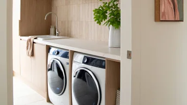 Laundry room with wood cabinets, washer, dryer, sink, and a vase with green leaves on the countertop.