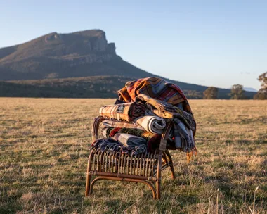 A stack of blankets on a cane chair with a mountain range in the distance.
