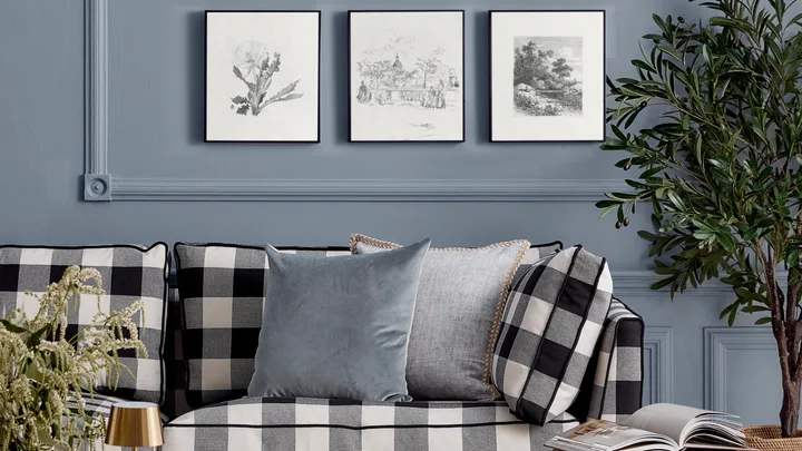 Black and white chequered couch in front of a blue wall with black and white artworks arranged in a grid pattern