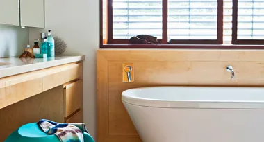 Modern bathroom with wooden accents, a freestanding tub, and toiletries on a countertop.