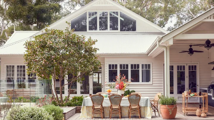 An exterior photo of a white house with an outdoor dining area with rattan styling
