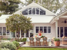 An exterior photo of a white house with an outdoor dining area with rattan styling