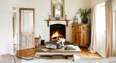 Cozy living room with a lit fireplace, rustic furniture, wooden floors, and a large mirror above the mantel.