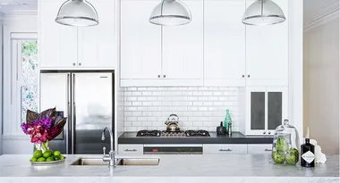 Modern kitchen with white cabinets, marble countertops, stainless steel appliances, flowers, and green limes.