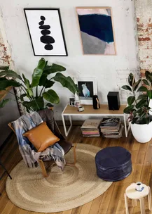 Cozy living room with plants, a leather chair with pillows, abstract wall art, and a small white table with decor.