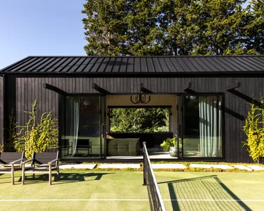 A tennis court beside a black cladded garden pavilion.
