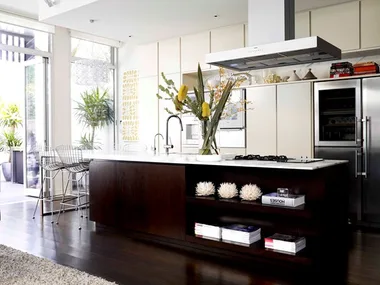 Modern kitchen with dark wood island, white countertops, stainless steel appliances, and large vase of flowers.