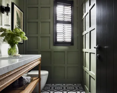 A forest green powder room with a mosaic tiled floor.