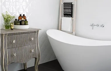 Luxurious bathroom with a freestanding white tub, striped cabinet with toiletries, and a towel ladder.