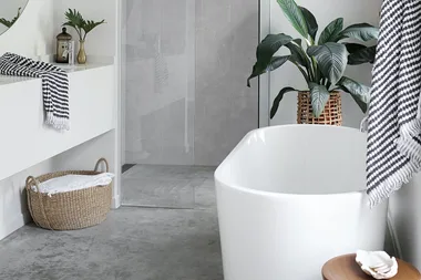 Modern bathroom with a white freestanding bathtub, wicker basket, indoor plant, and black-and-white striped towel.