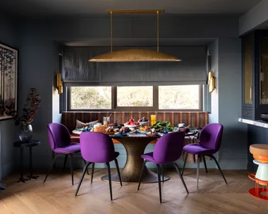 A dining nook with purple chairs, a mixed patterned bench seat and a brass pendant.
