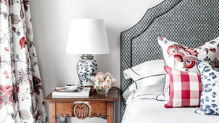 A guest bedroom with floral curtains, a timber side table and grey lined bedhead.