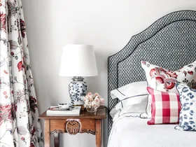 A guest bedroom with floral curtains, a timber side table and grey lined bedhead.