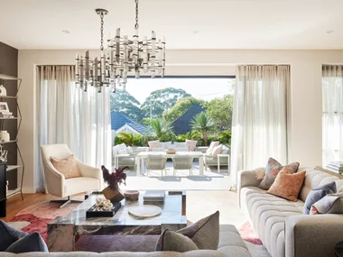 An open plan living room with a grey couch, marble coffee table and one wall painted white and one wall painted black. The sliding door opens to an outdoor living area.