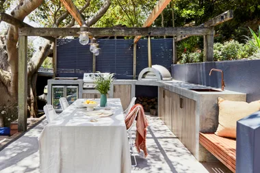 An outdoor kitchen with a concrete bench, pizza oven and hanging festoon lights.