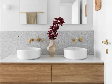 A white and grey ensuite with a timber vanity, gold tapware and arched mirrors.