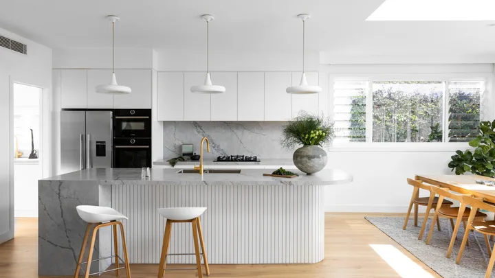 A white coastal-style kitchen with a fluted island and grey marble.