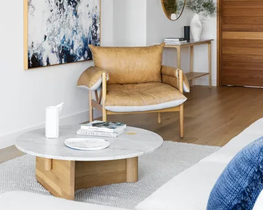 A white living area with a tan leather chair beside an abstract artwork.