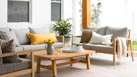 Outdoor patio with grey sofas, yellow cushions, wooden coffee table, and plants; lemonade and salad on table.