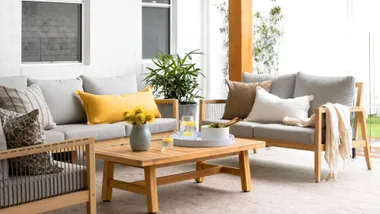 Outdoor patio with grey sofas, yellow cushions, wooden coffee table, and plants; lemonade and salad on table.