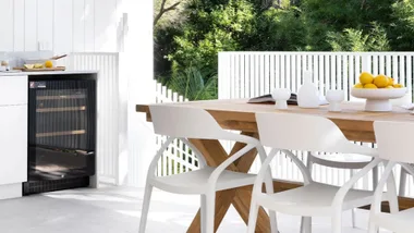Outdoor dining area with wooden table, white chairs, and lemons on a platter. A small fridge is visible under the counter.