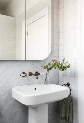 Bathroom sink with brass taps, a decorative vase with flowers, and a green towel.