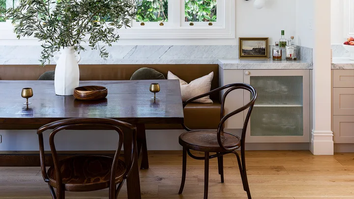 Dark brown leather banquette seating with a large dining table and dining chairs against a white wall