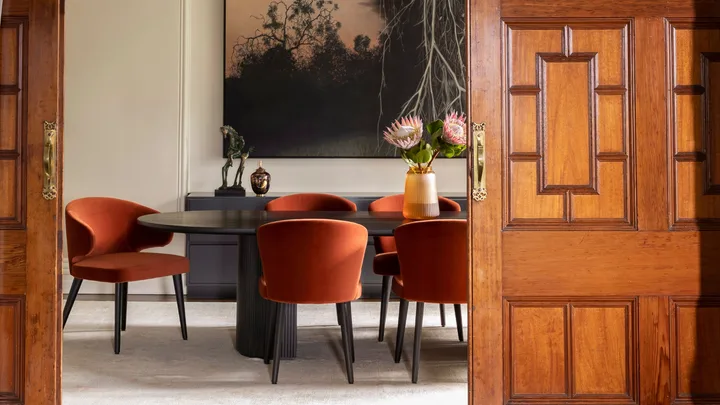 dining area posted behind a wooden door with rust-coloured dining chairs around a rectangular table